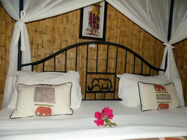 Double bed with elephant cushions under a white canopy against bamboo walls
